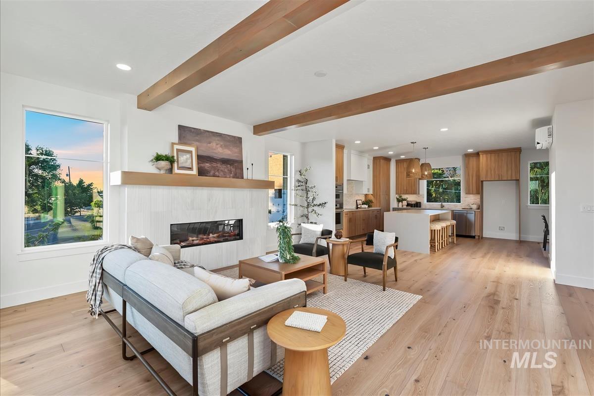 Bright living space featuring wood-finish flooring, a linear fireplace with a textured surround, and exposed ceiling beams