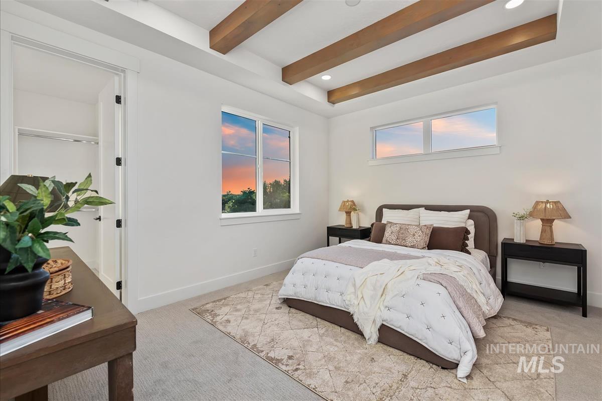 Bright bedroom with exposed wood ceiling beams, recessed lighting, and a large window providing ample natural light