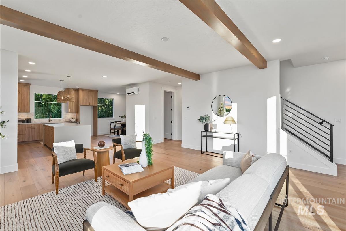 Expansive main living space featuring exposed wood ceiling beams, light wood-finish flooring, and a modern open-tread staircase with horizontal metal railings