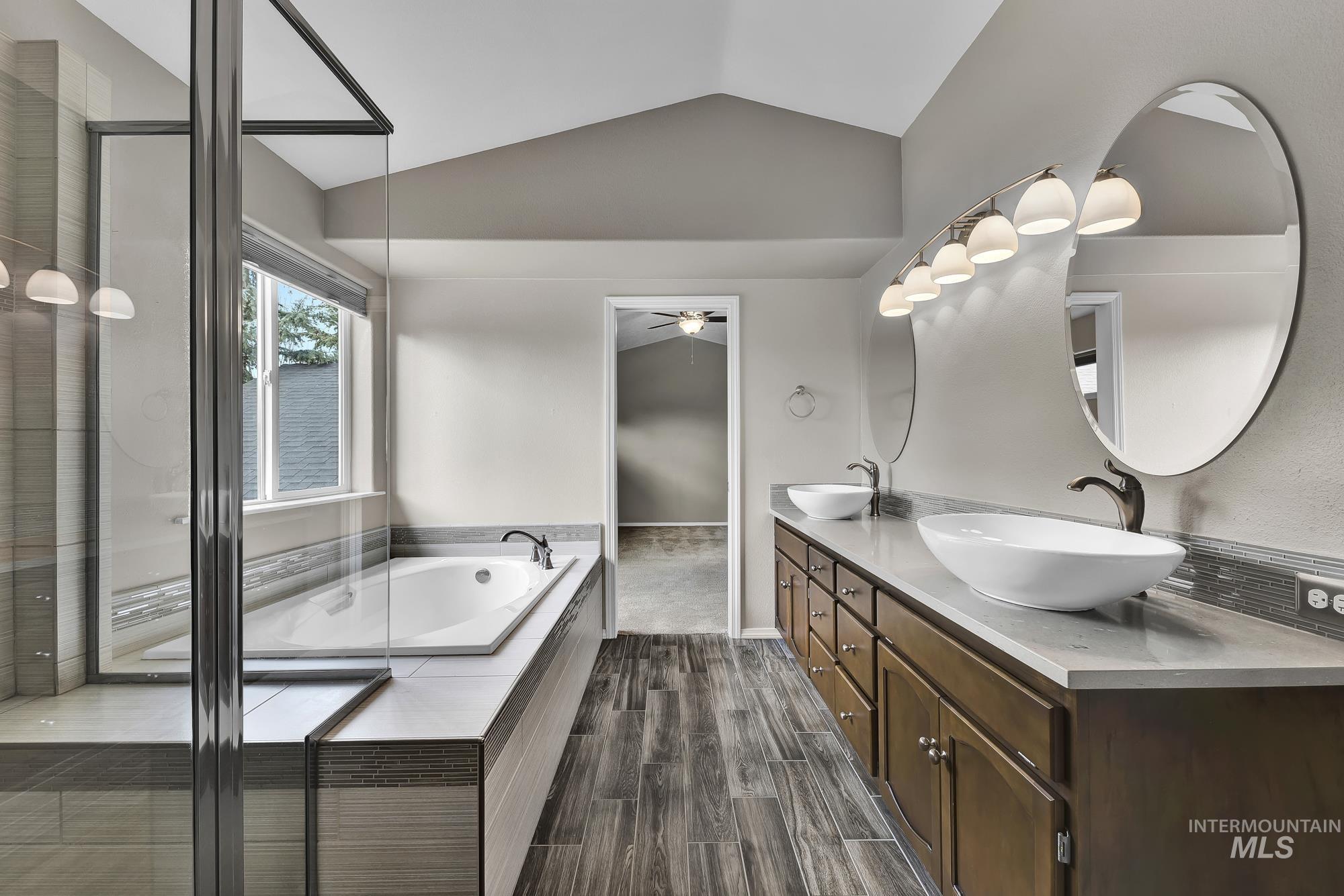 Bathroom featuring vaulted ceiling, double vanity, a bath, dark wood-style flooring, and an enclosed shower