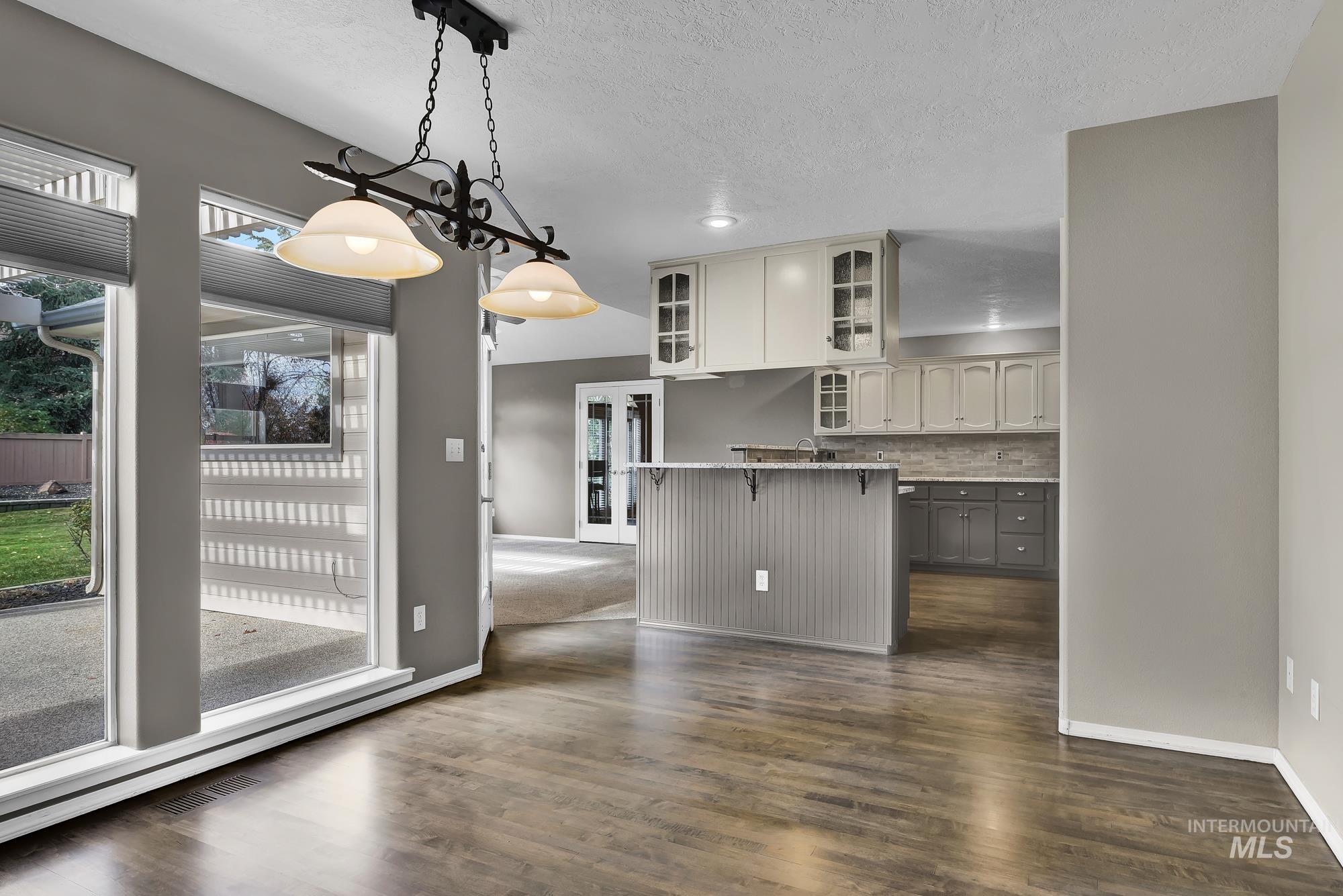 Kitchen featuring a kitchen bar, hanging light fixtures, glass insert cabinets, a baseboard radiator, and dark wood-style flooring