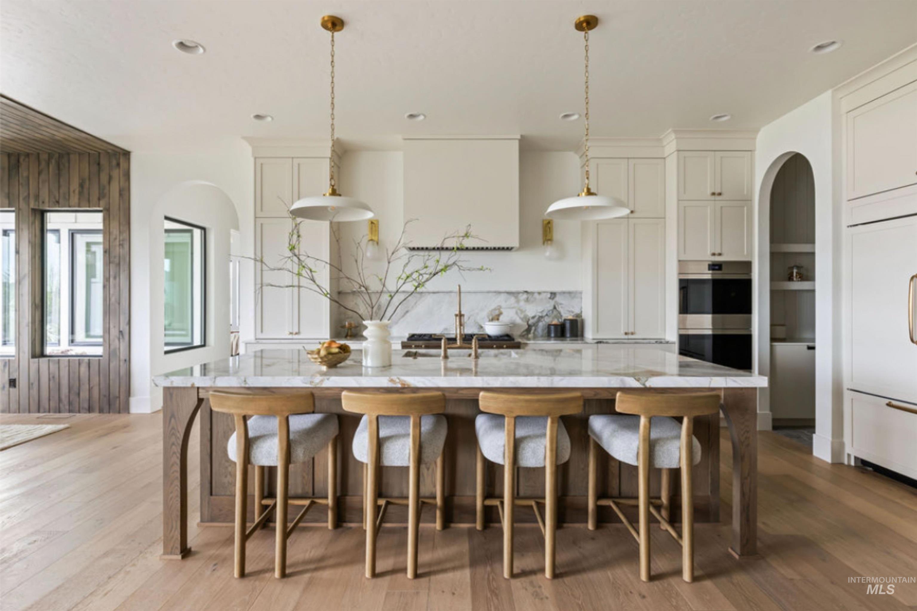 Kitchen with arched walkways, paneled fridge, light stone counters, light wood finished floors, and recessed lighting