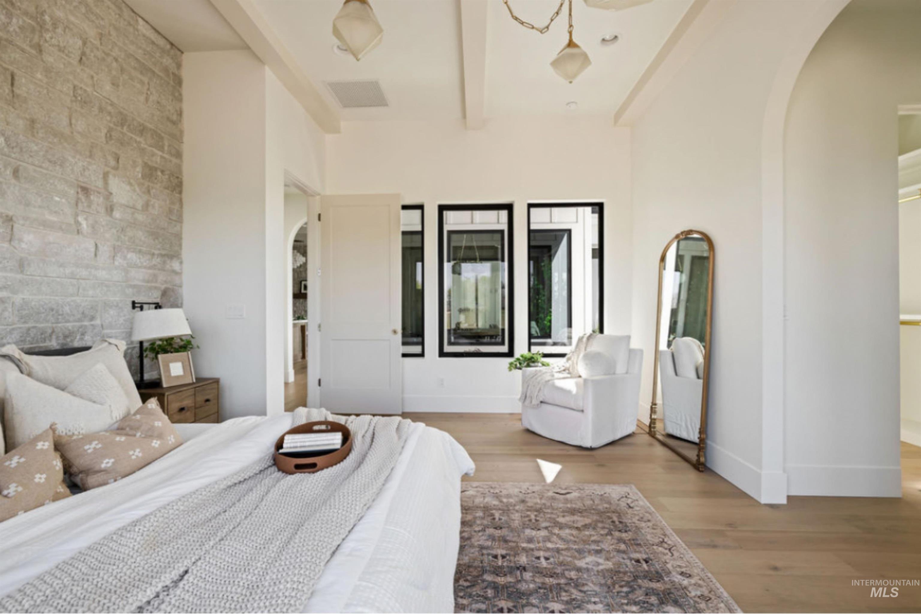 Bedroom with arched walkways, beam ceiling, and wood finished floors
