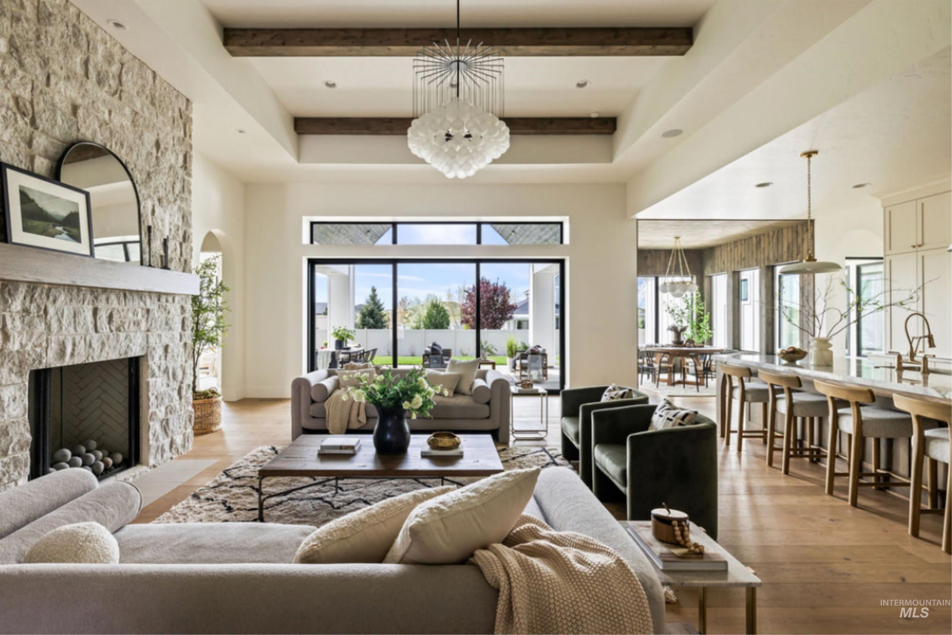 Living area with light wood-style floors, beamed ceiling, a stone fireplace, a chandelier, and a towering ceiling