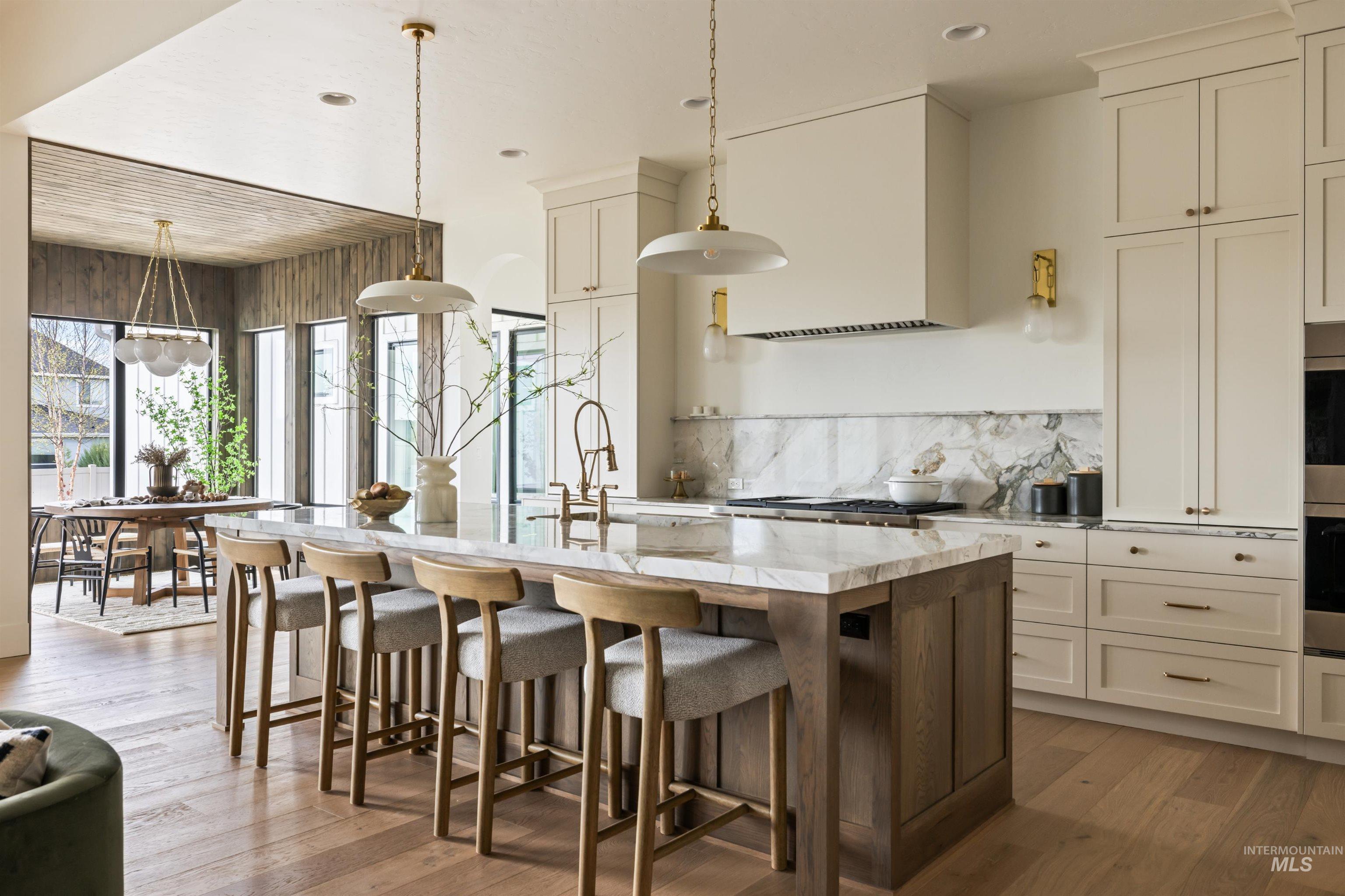 Kitchen featuring light stone counters, a breakfast bar, hanging light fixtures, backsplash, and light wood-style flooring