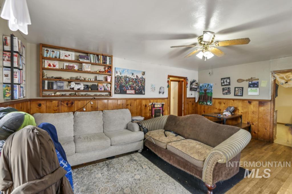 Living area with wood walls, wainscoting, ceiling fan, and wood finished floors