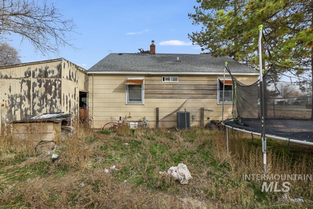 Back of house with a trampoline, a shingled roof, and a chimney