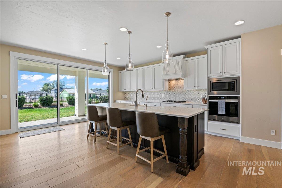 Kitchen with stainless steel appliances, white cabinets, backsplash, a breakfast bar, and hanging light fixtures