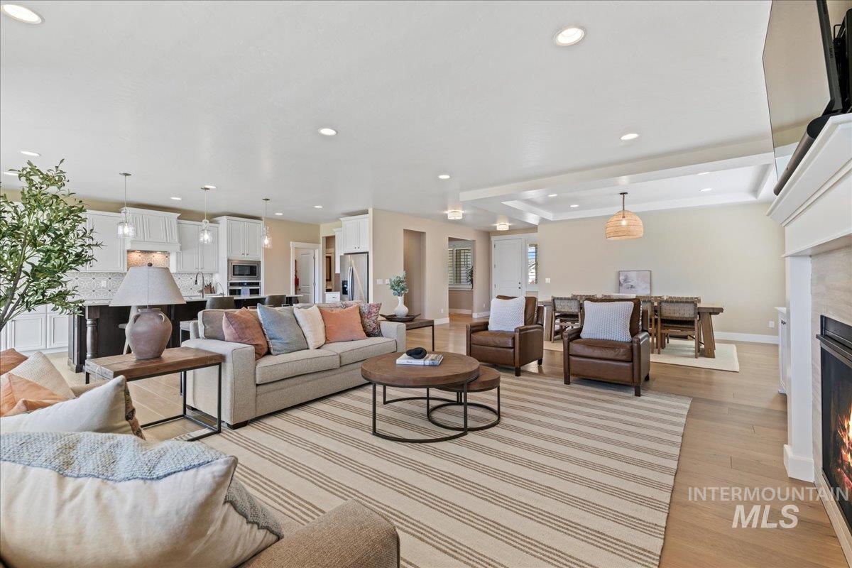 Living area featuring a raised ceiling, a warm lit fireplace, recessed lighting, and light wood-type flooring