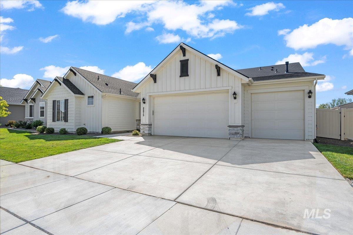 Modern farmhouse style home featuring board and batten siding, driveway, an attached garage, a front lawn, and roof with shingles