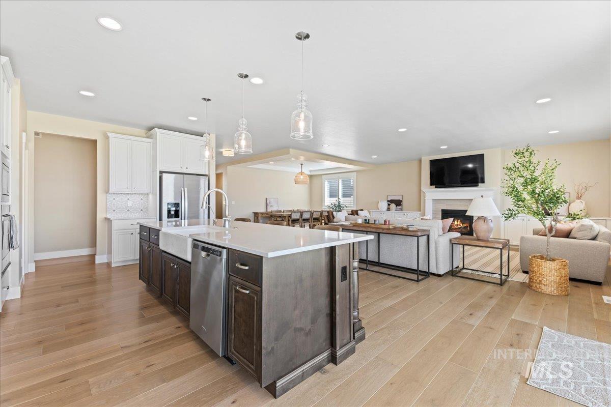 Kitchen with dark brown cabinetry, open floor plan, hanging light fixtures, white cabinetry, and appliances with stainless steel finishes