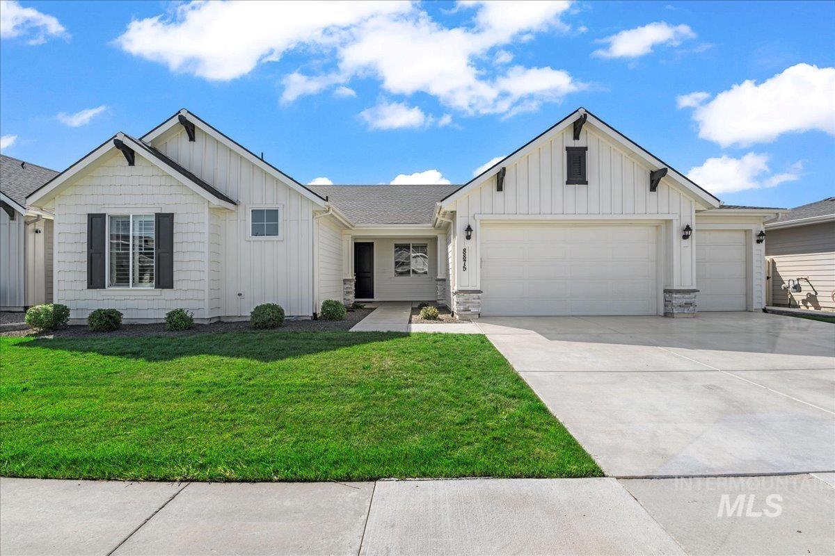 View of front of property featuring board and batten siding, a garage, concrete driveway, a front lawn, and stone siding