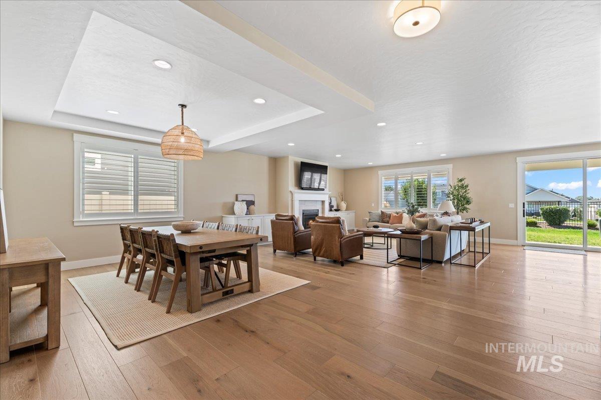 Dining room with light wood-style flooring, a fireplace, a tray ceiling, and recessed lighting