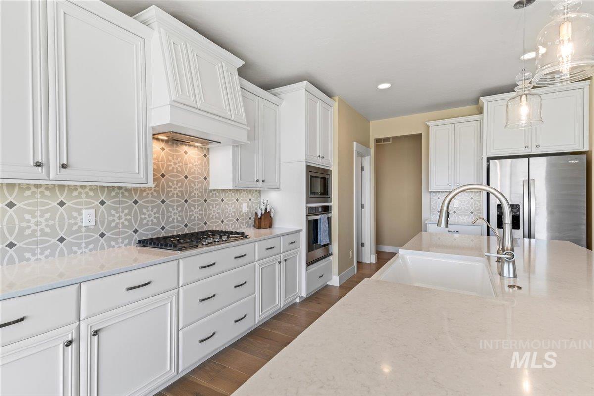 Kitchen featuring stainless steel appliances, light stone counters, hanging light fixtures, decorative backsplash, and recessed lighting