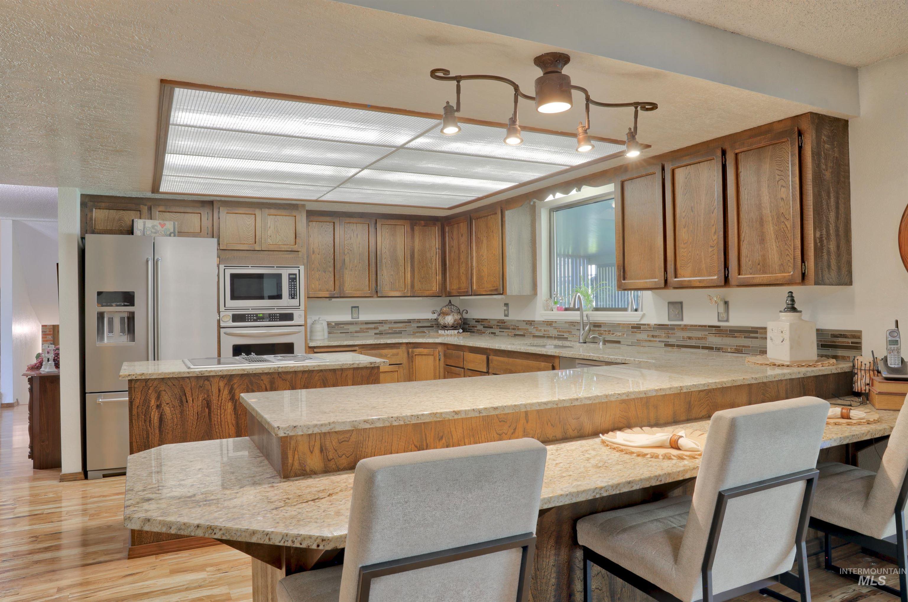 Kitchen with light stone countertops, stainless steel appliances, brown cabinets, a textured ceiling, and light wood-type flooring
