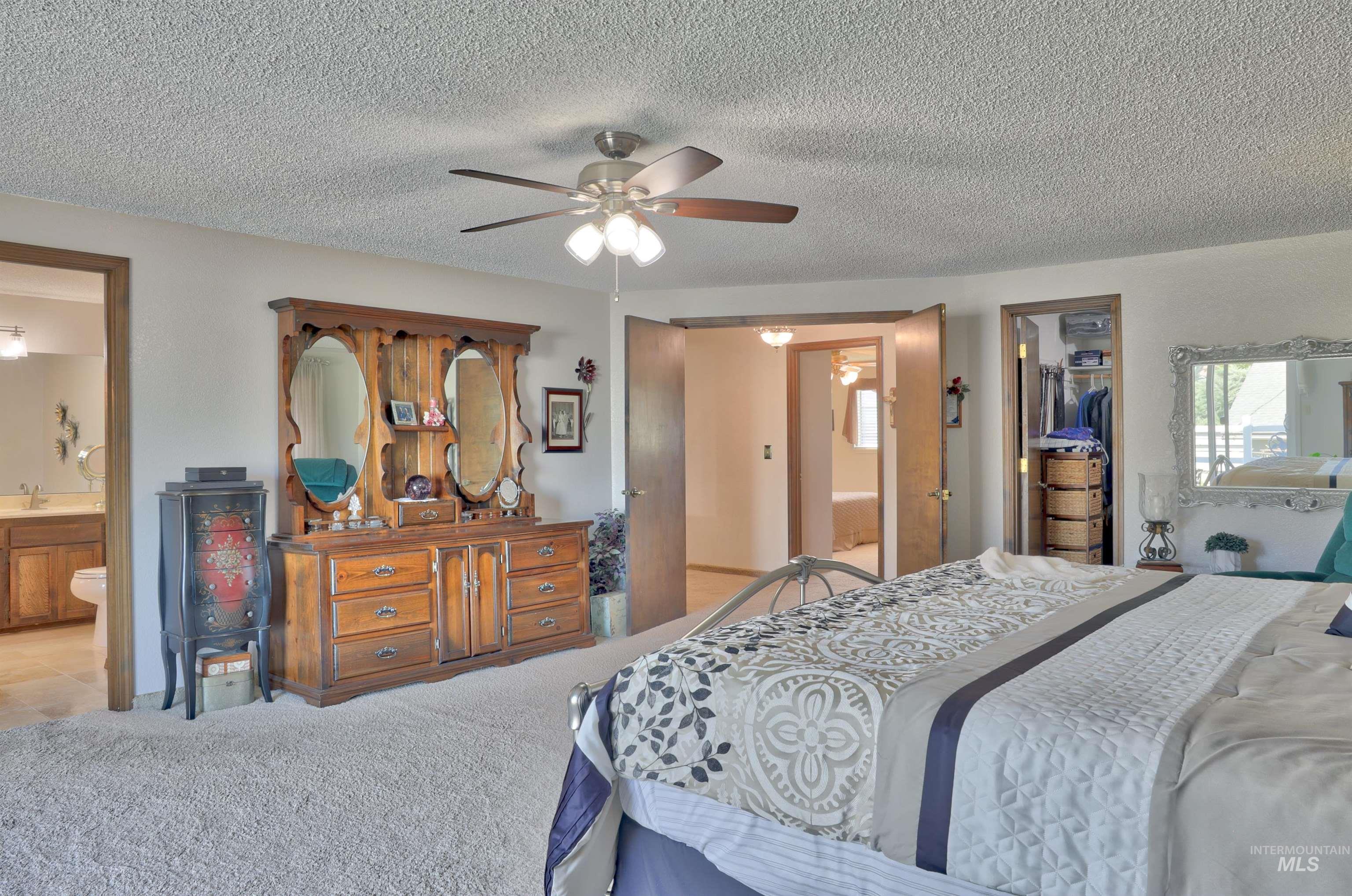 Bedroom with ensuite bathroom, carpet flooring, a textured ceiling, ceiling fan, and a walk in closet,