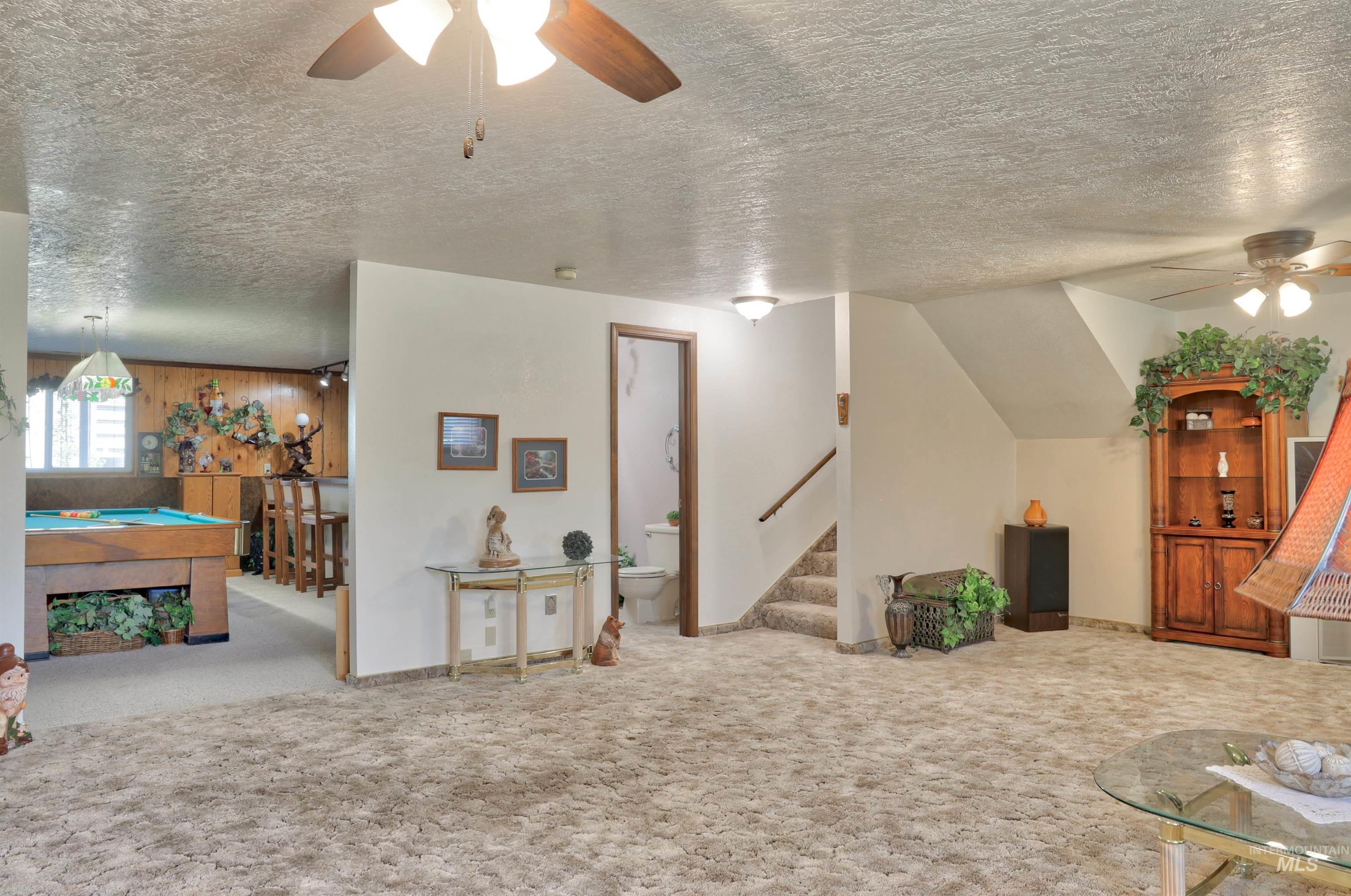 Carpeted living area with ceiling fan, pool table, a textured ceiling, and stairway