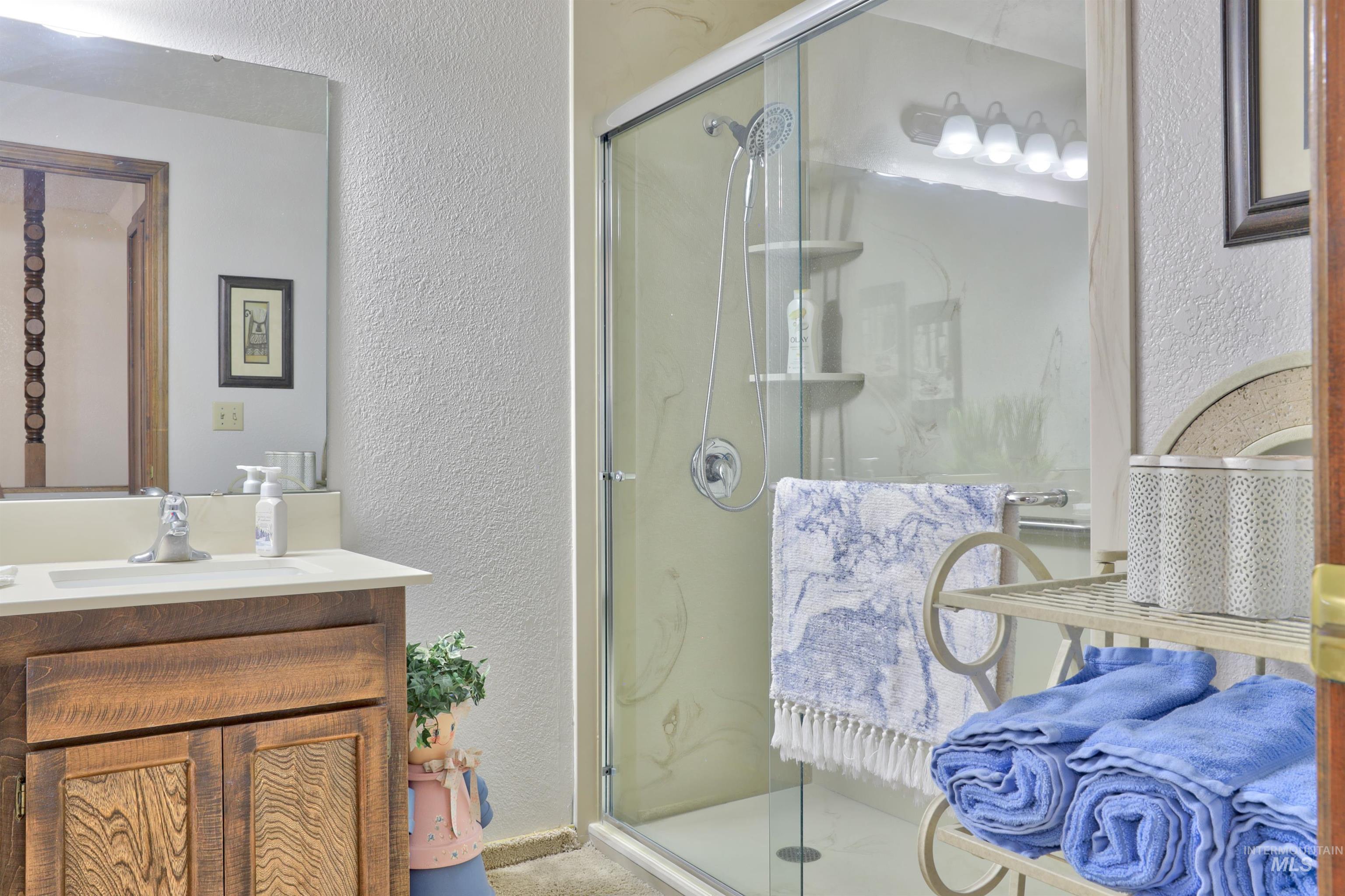 Full bathroom with a textured wall, vanity, and a shower stall