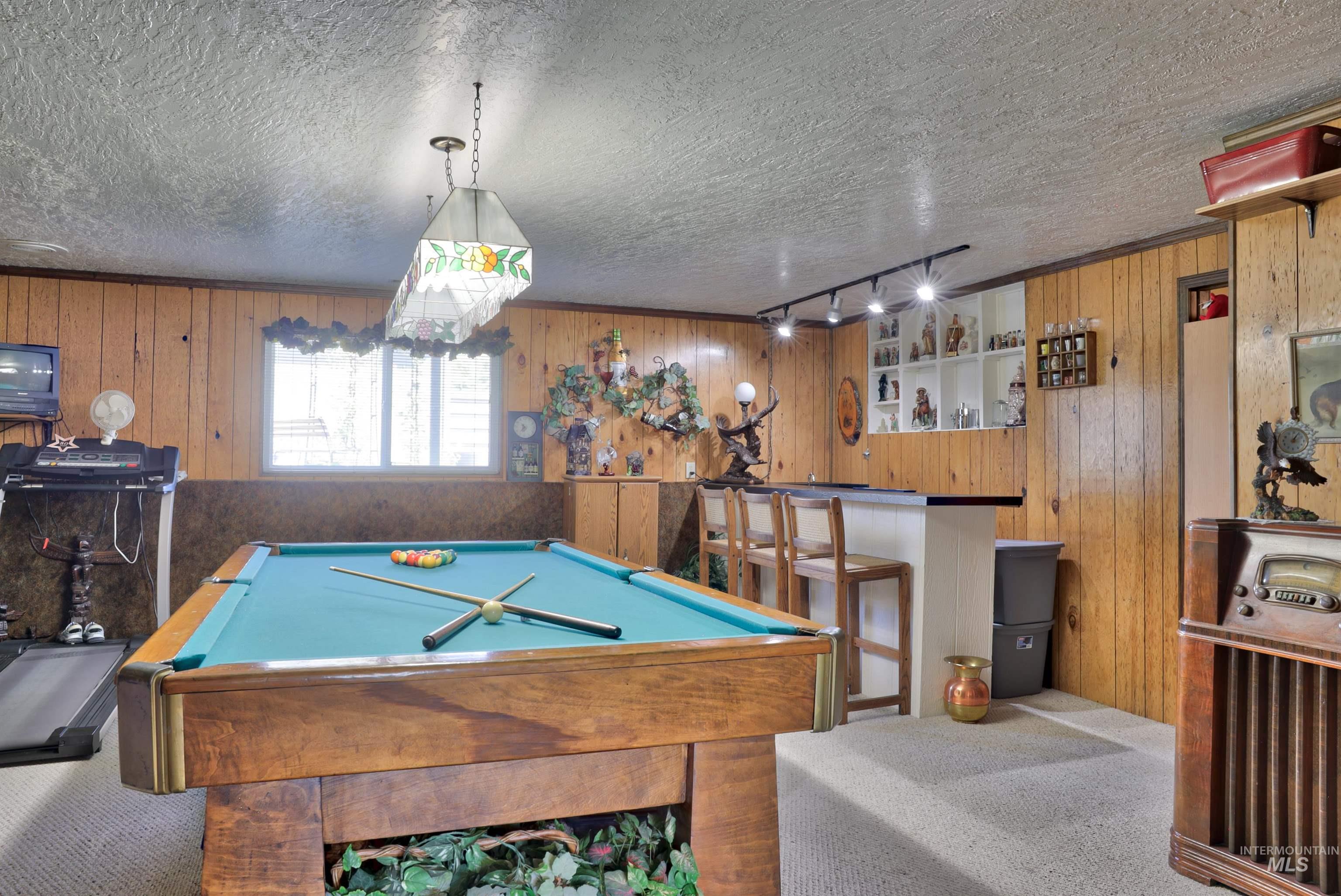 Rec room with carpet flooring, pool table, wood walls, and a textured ceiling
