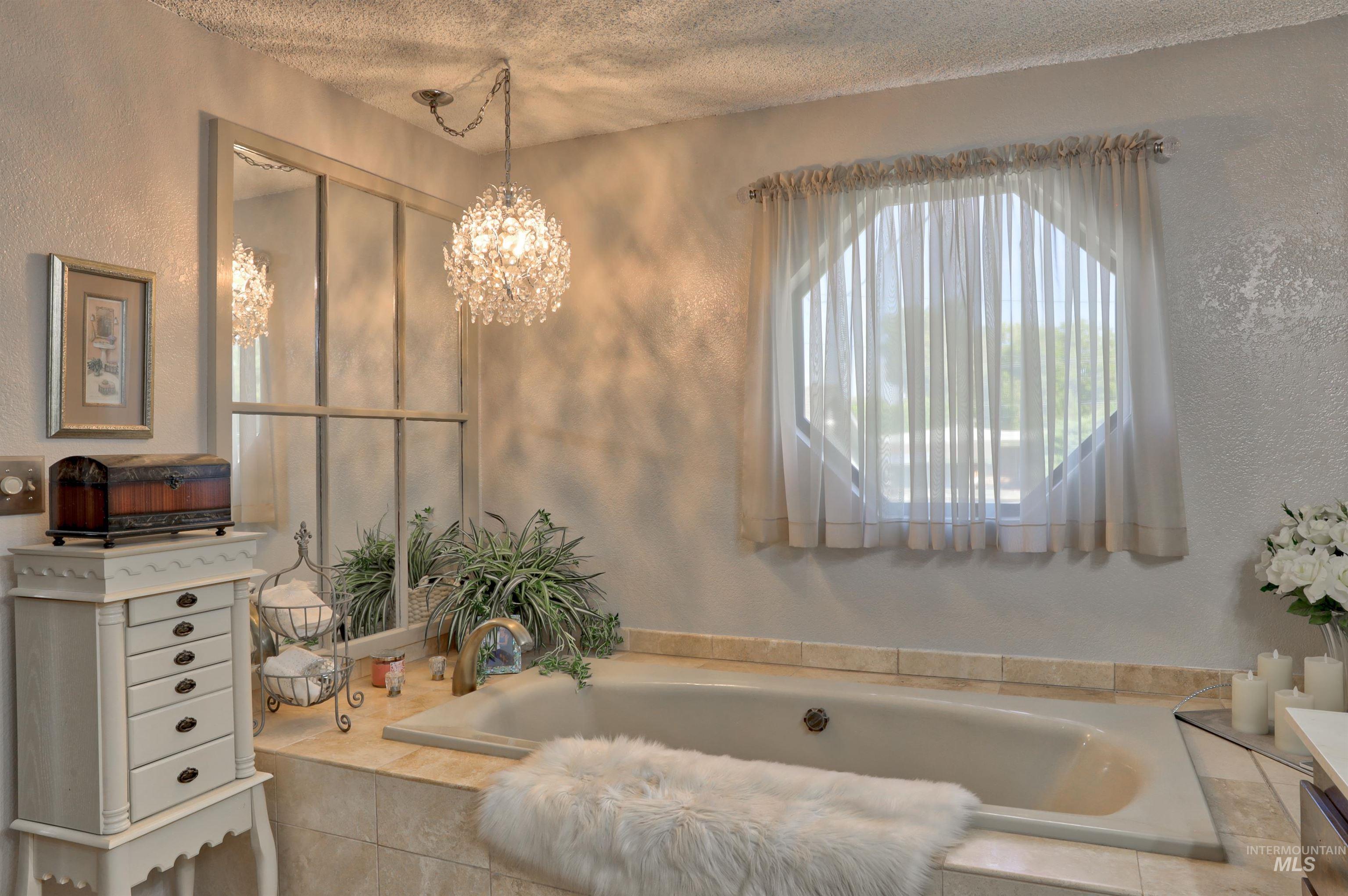 Full bathroom featuring a textured wall, a garden tub, a chandelier, and a textured ceiling