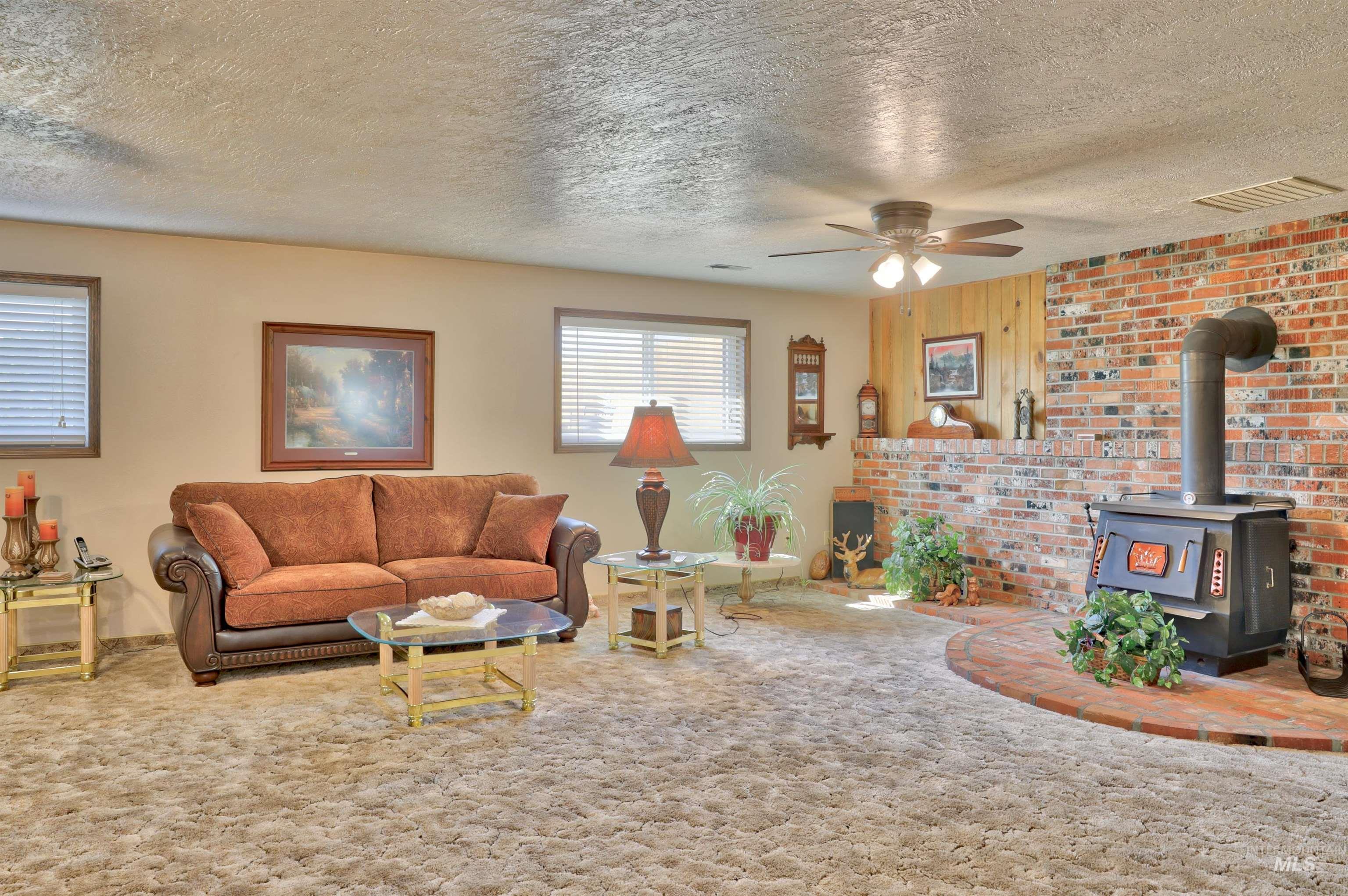 Living room with a wood stove, carpet flooring, a textured ceiling, and a ceiling fan