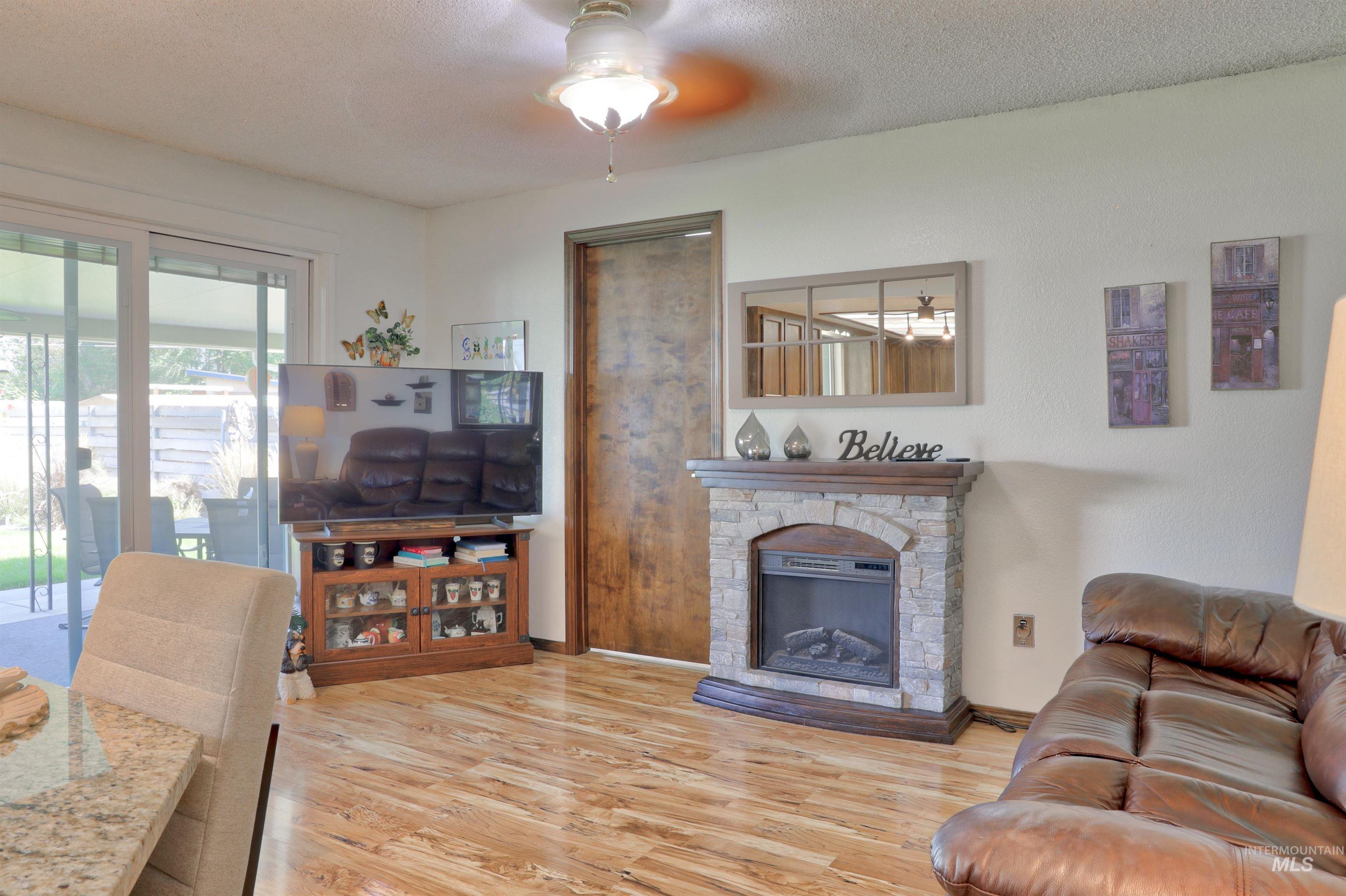 Living room featuring light wood-type flooring, a textured ceiling, a stone fireplace, and a ceiling fan