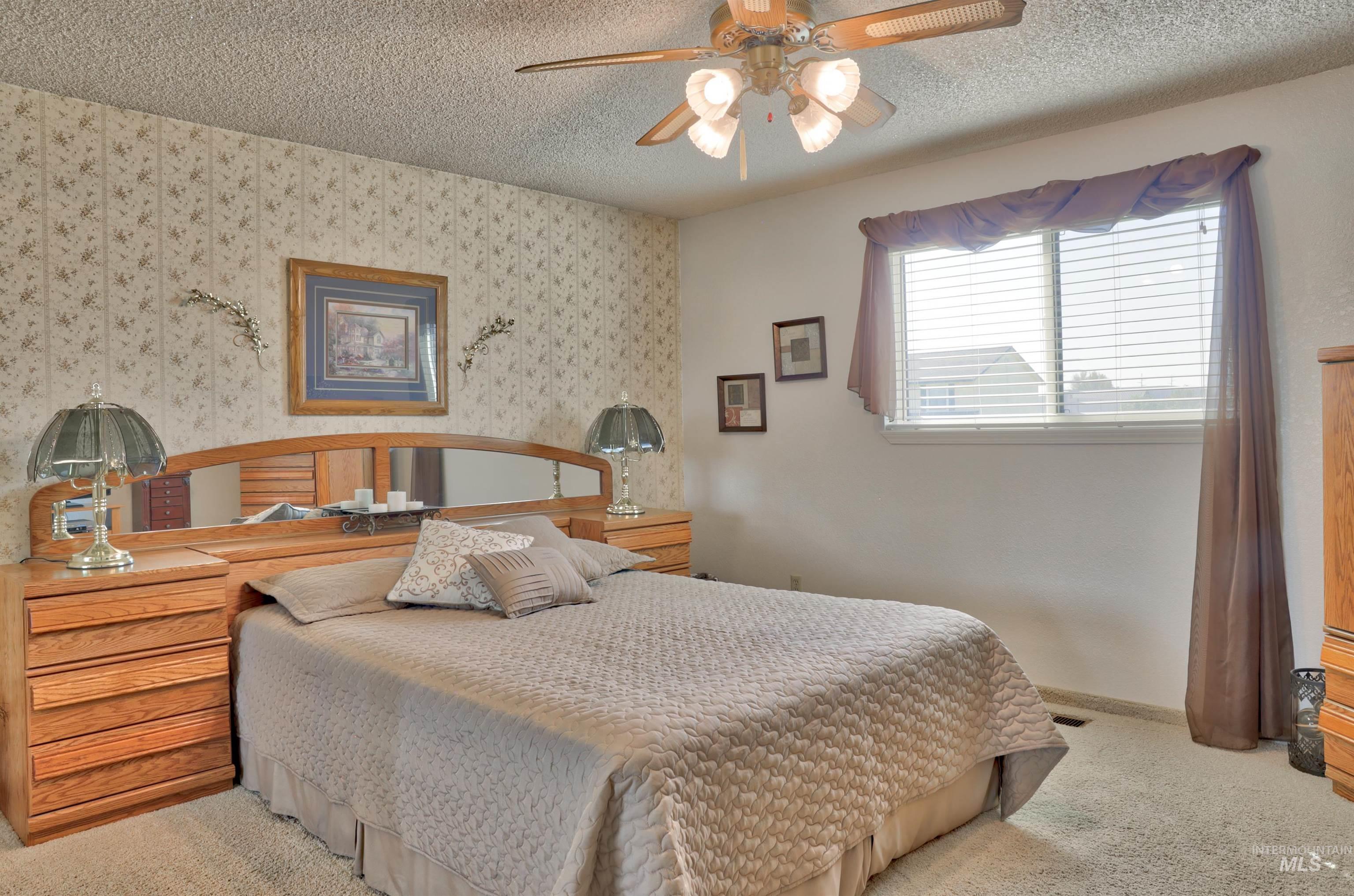 Carpeted bedroom with ceiling fan and a textured ceiling sliding door to a sitting deck.