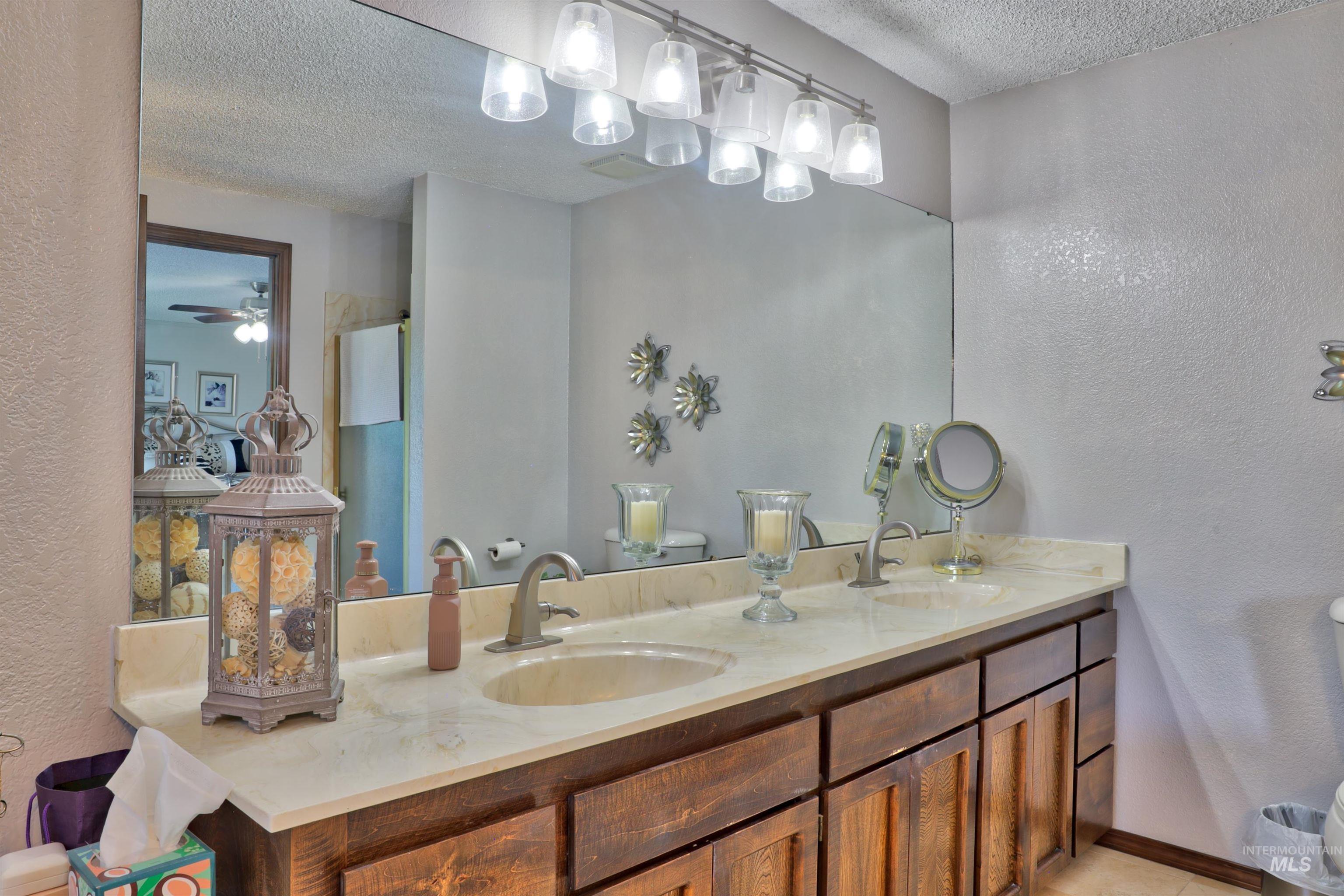 Full bath featuring a textured wall, a textured ceiling, double vanity,