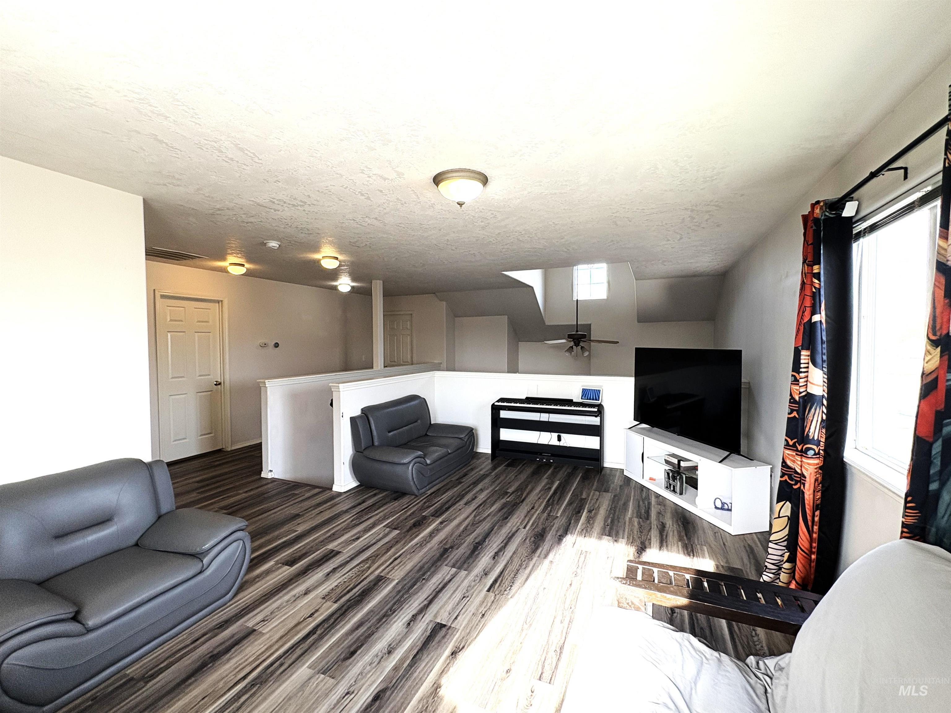 Living area with dark wood-type flooring, a textured ceiling, a ceiling fan, and a skylight