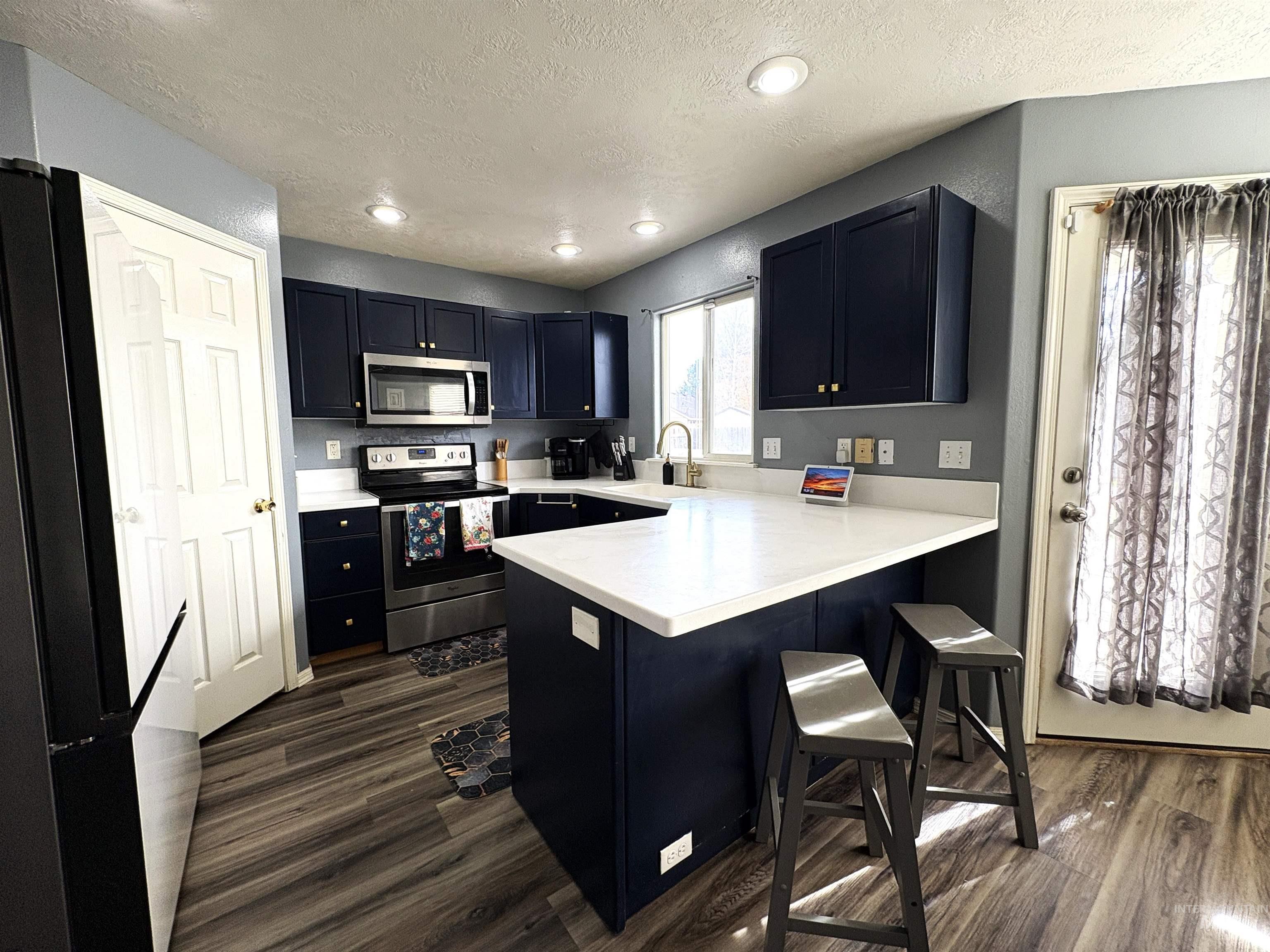Kitchen featuring light countertops, stainless steel appliances, a peninsula, a breakfast bar, and a textured ceiling