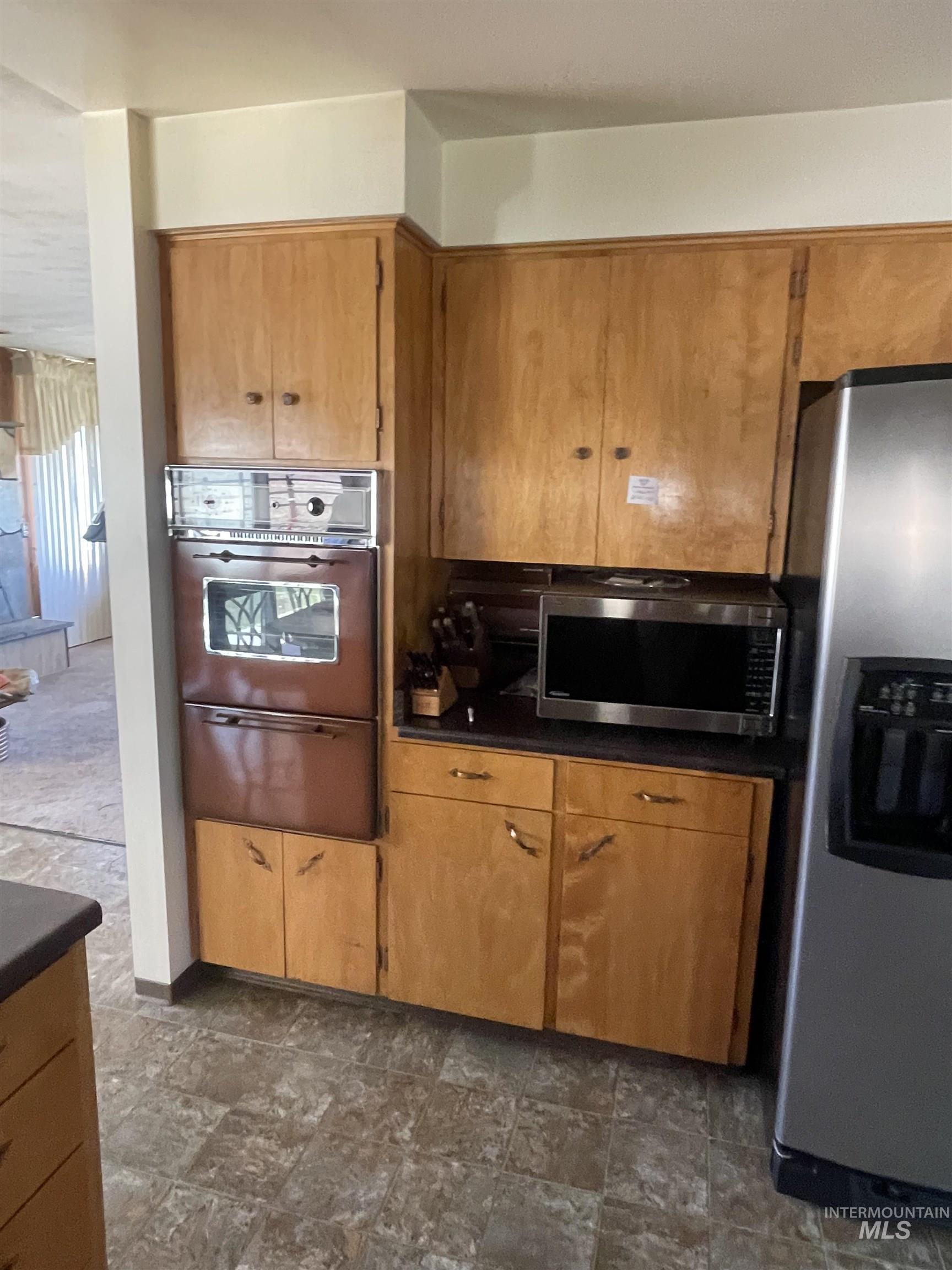 Kitchen featuring dark countertops, stainless steel appliances, a warming drawer, and brown cabinets