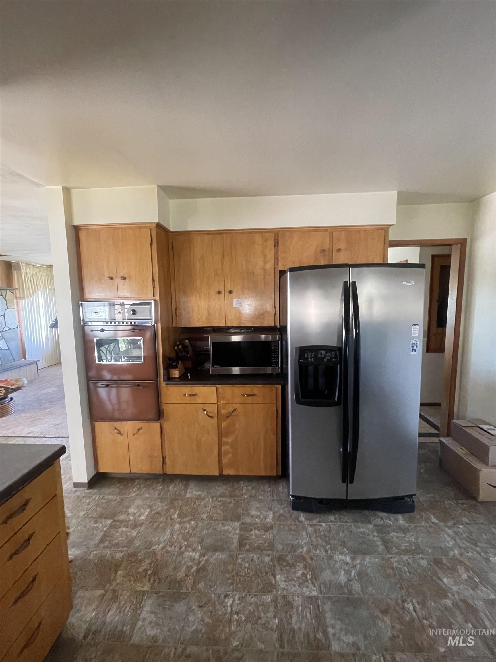 Kitchen with appliances with stainless steel finishes, stone finish floors, brown cabinets, dark countertops, and a warming drawer