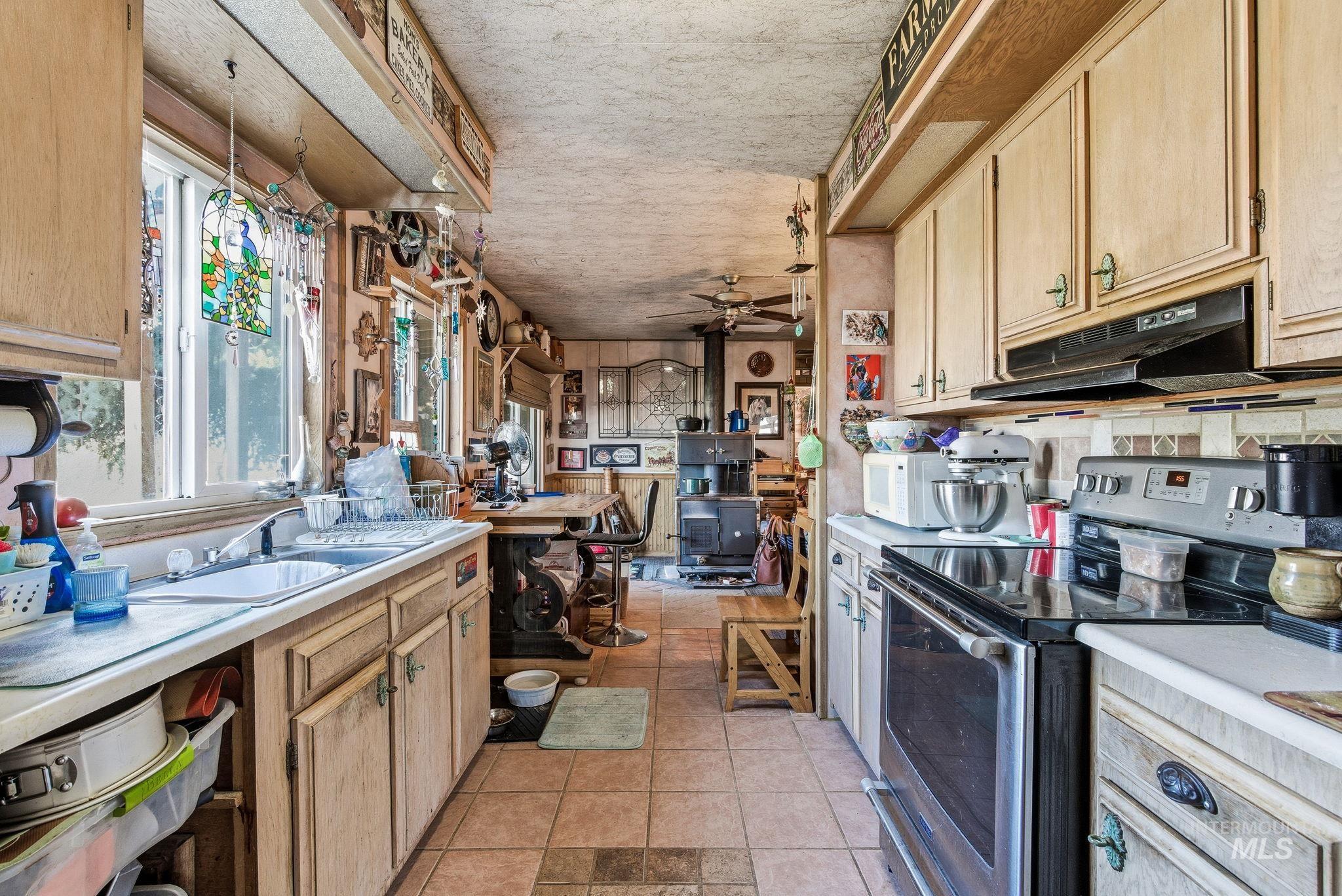 Kitchen with light brown cabinetry, stainless steel range with electric cooktop, light countertops, and a ceiling fan