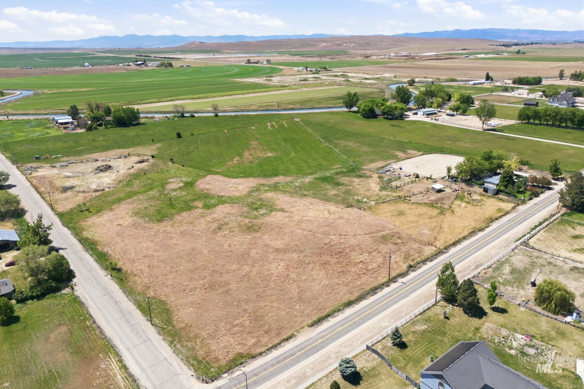 Expansive undeveloped land parcel featuring a paved road frontage, partially fenced perimeter, and distant mountain backdrops
