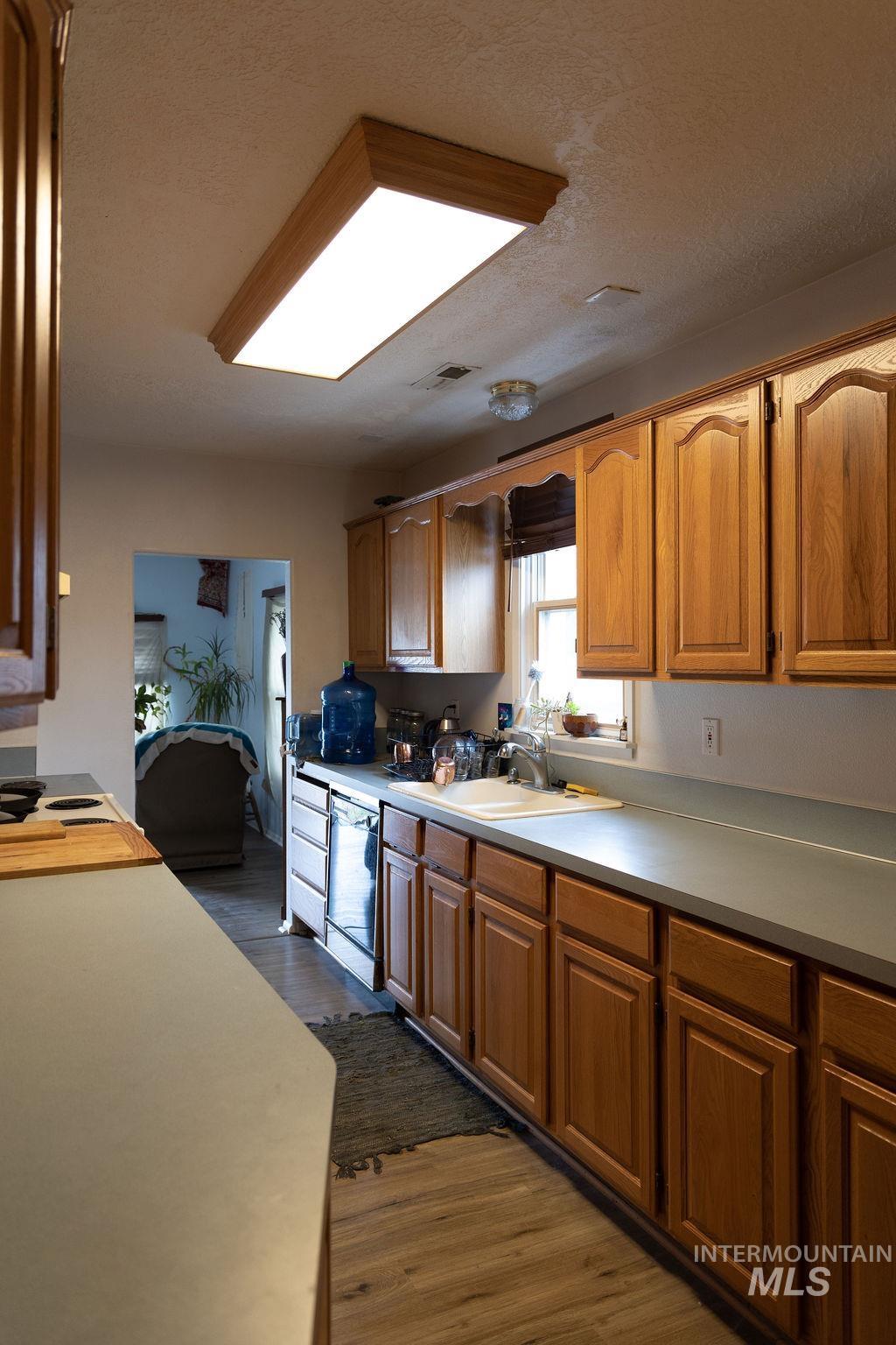 Kitchen with dark wood-type flooring, light countertops, brown cabinets, and a textured ceiling