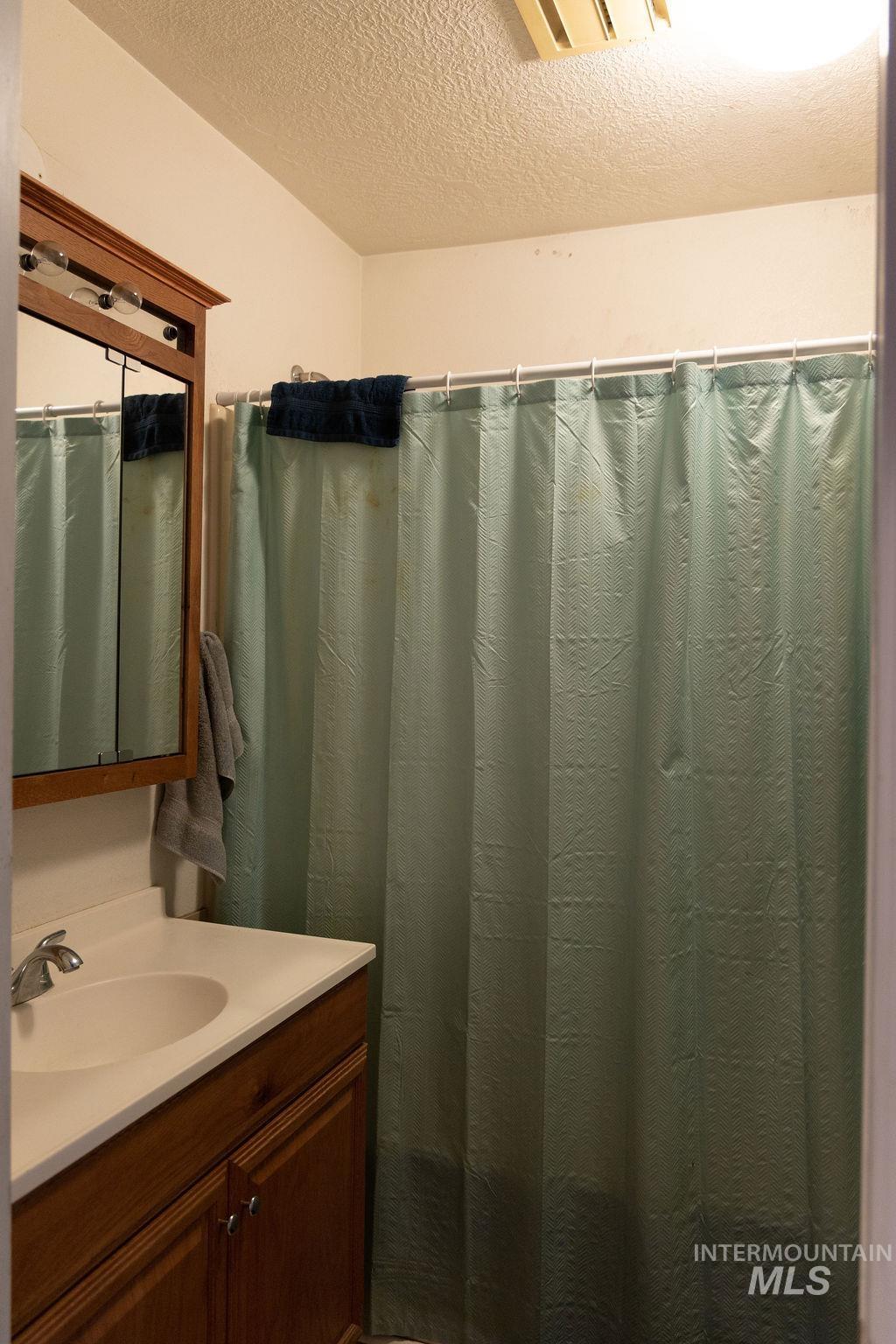 Bathroom featuring a textured ceiling, vanity, and curtained shower