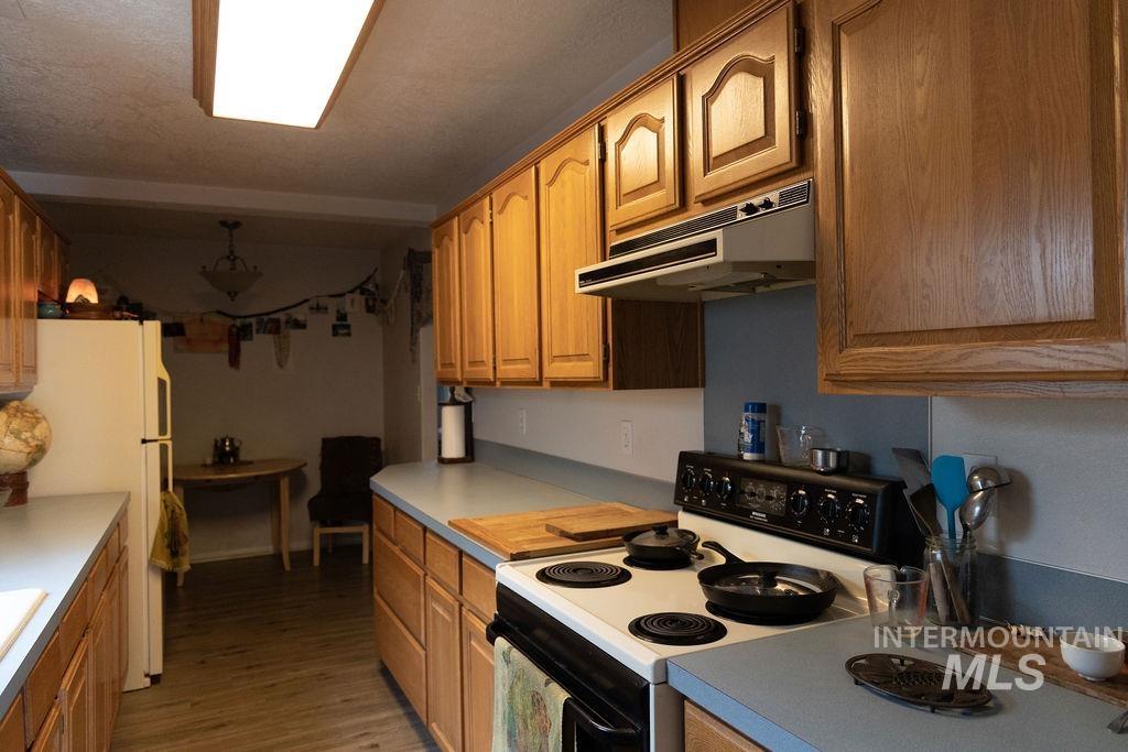 Kitchen featuring electric stove, under cabinet range hood, freestanding refrigerator, dark wood finished floors, and light countertops