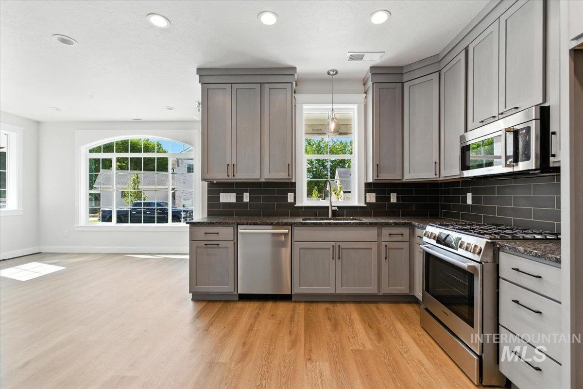 Kitchen with stainless steel appliances, light wood finished floors, gray cabinetry, backsplash, and plenty of natural light