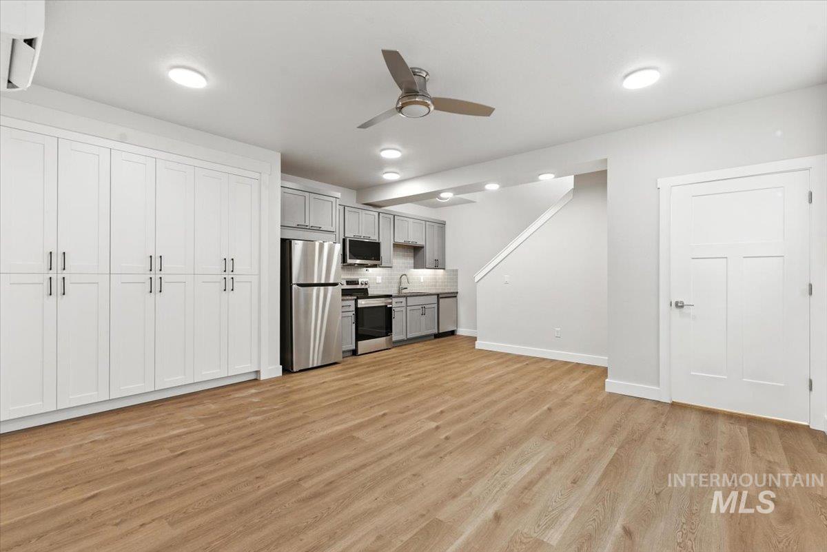 Kitchen featuring stainless steel appliances, light wood-type flooring, an AC wall unit, tasteful backsplash, and ceiling fan