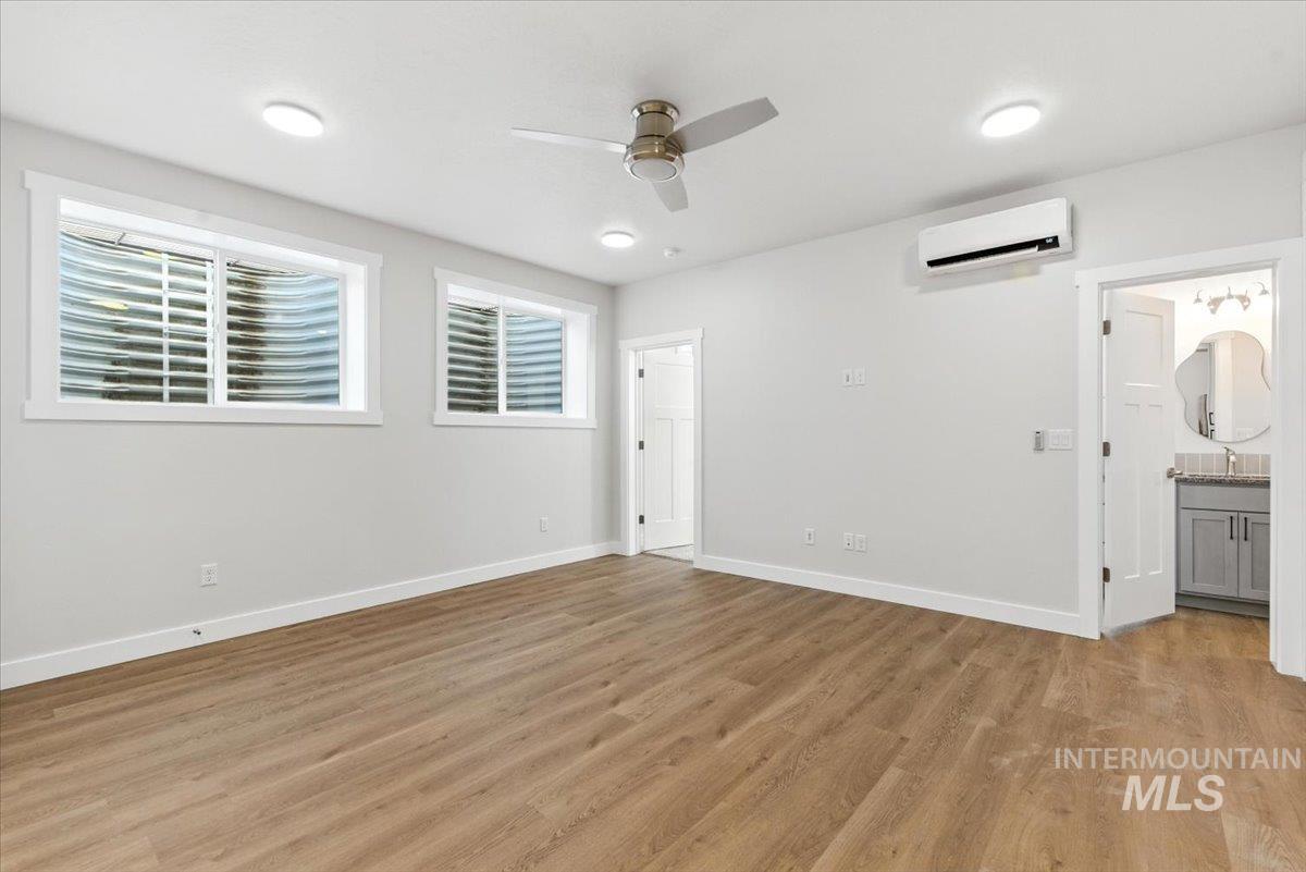 Unfurnished bedroom with an AC wall unit, light wood-style floors, ensuite bath, and a ceiling fan