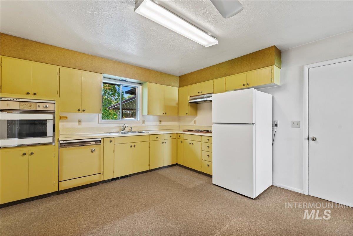 Kitchen with freestanding refrigerator, wall oven, light countertops, a textured ceiling, and under cabinet range hood
