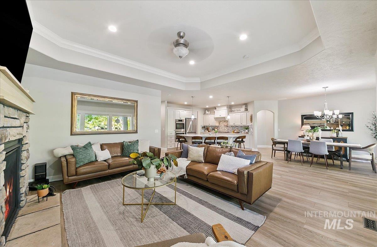 Living area with a stone fireplace, crown molding, recessed lighting, arched walkways, and a raised ceiling