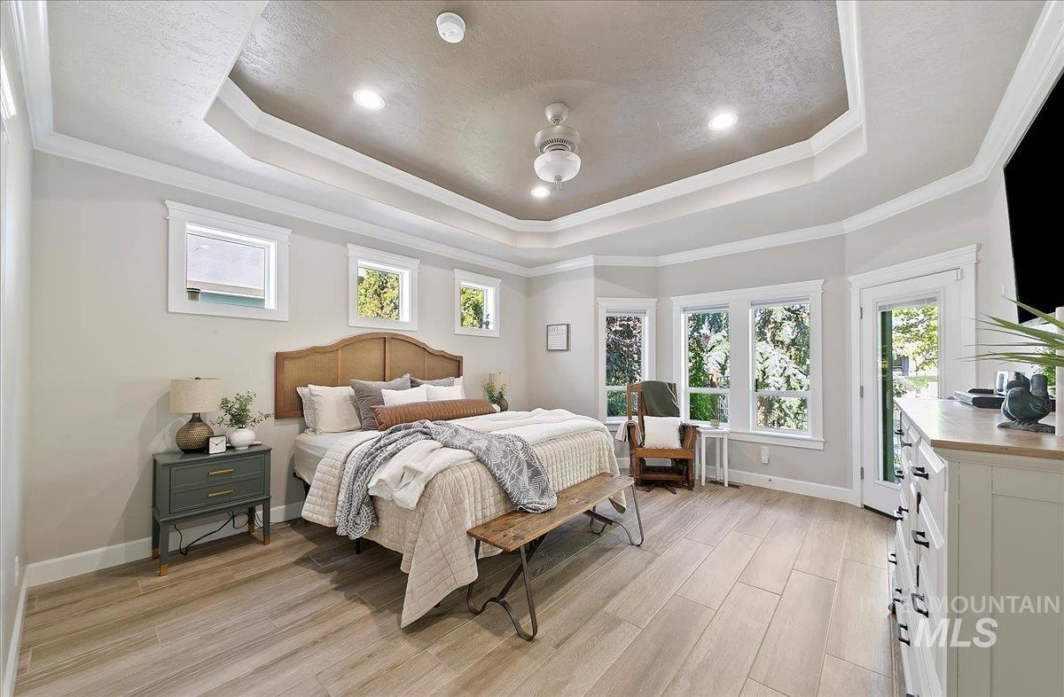 Bedroom with multiple windows, ornamental molding, light wood-type flooring, a raised ceiling, and access to exterior