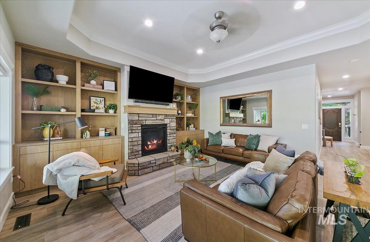 Living room featuring built in features, light wood-type flooring, recessed lighting, a tray ceiling, and ornamental molding