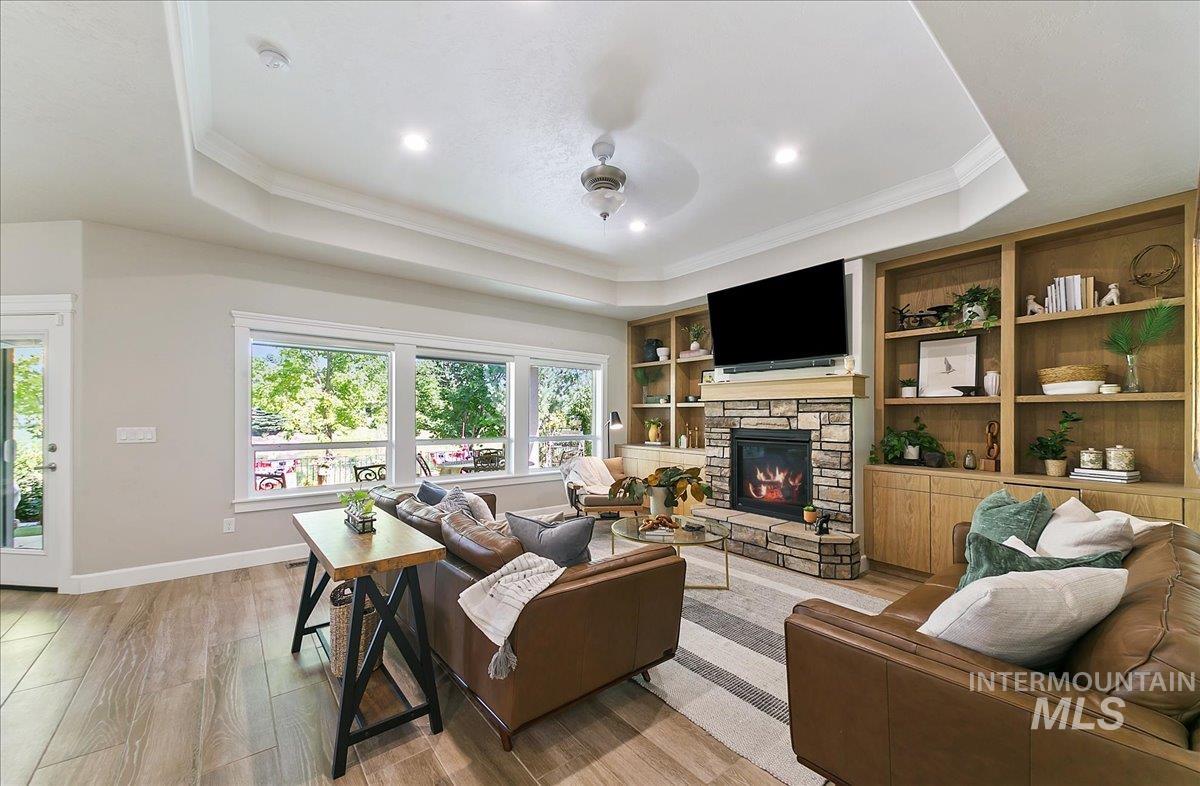 Living area featuring ornamental molding, a tray ceiling, light wood-type flooring, a ceiling fan, and a fireplace