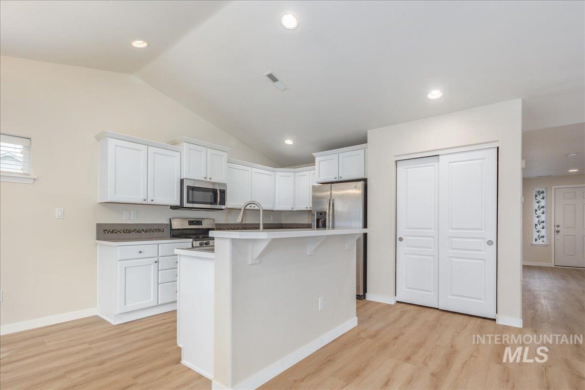 Kitchen with white cabinetry, lofted ceiling, light wood finished floors, appliances with stainless steel finishes, and recessed lighting