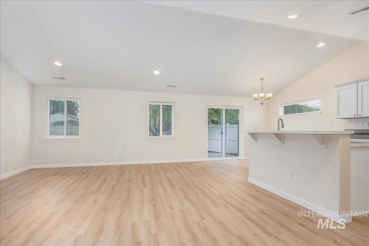 Unfurnished living room with recessed lighting, light wood-style flooring, a chandelier, healthy amount of natural light, and lofted ceiling