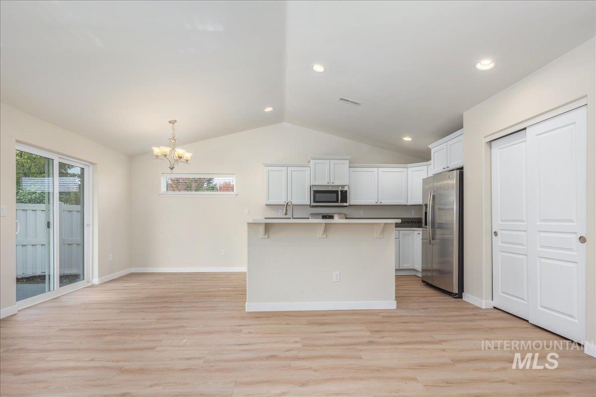 Kitchen with a kitchen breakfast bar, stainless steel appliances, white cabinets, light wood-style floors, and pendant lighting