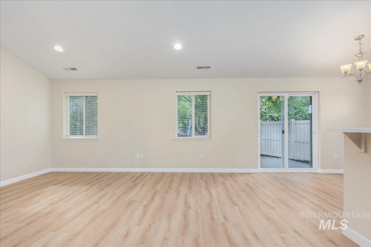 Empty room with light wood-style flooring, plenty of natural light, recessed lighting, and a chandelier