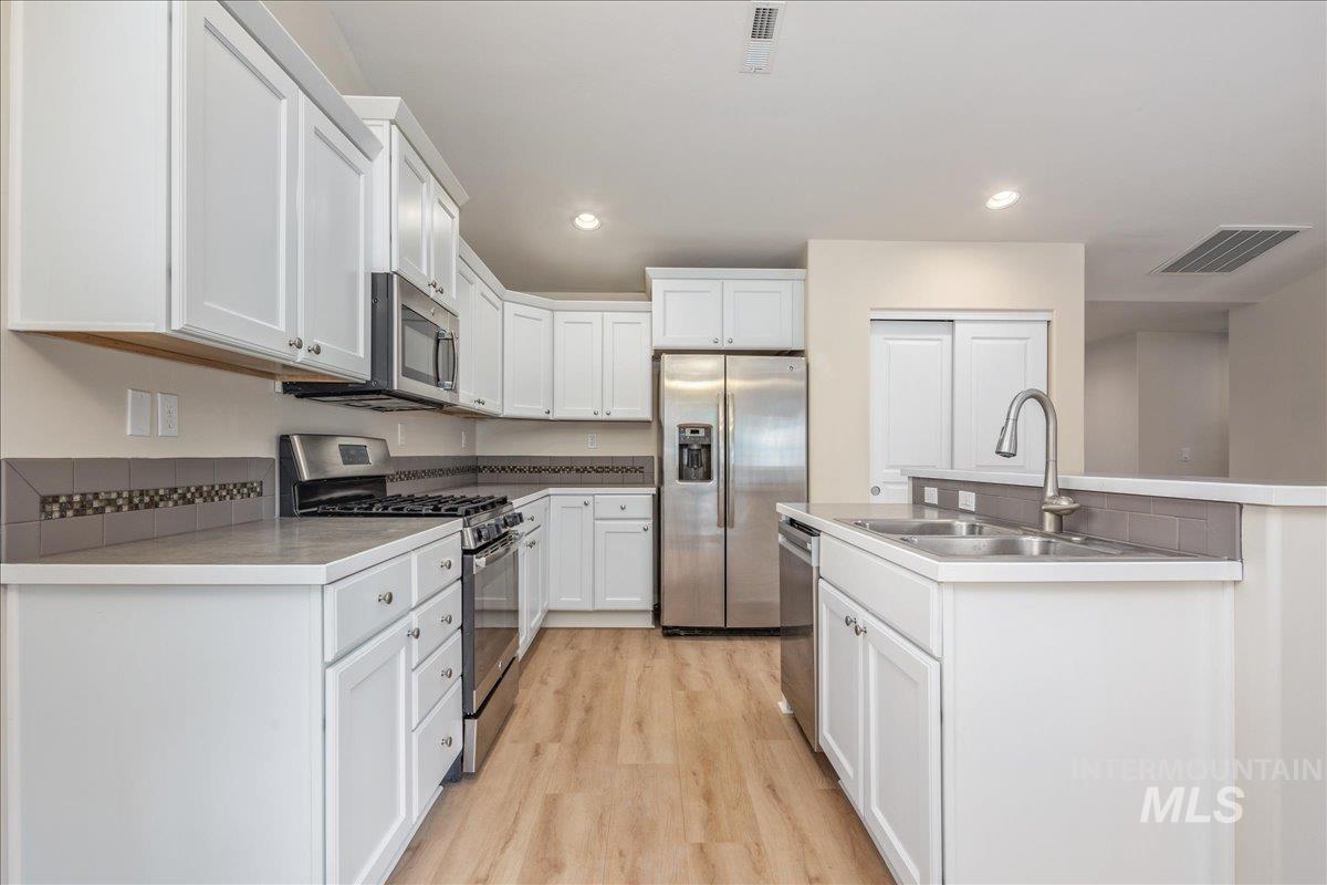 Kitchen with stainless steel appliances, a center island with sink, white cabinetry, light wood-type flooring, and recessed lighting